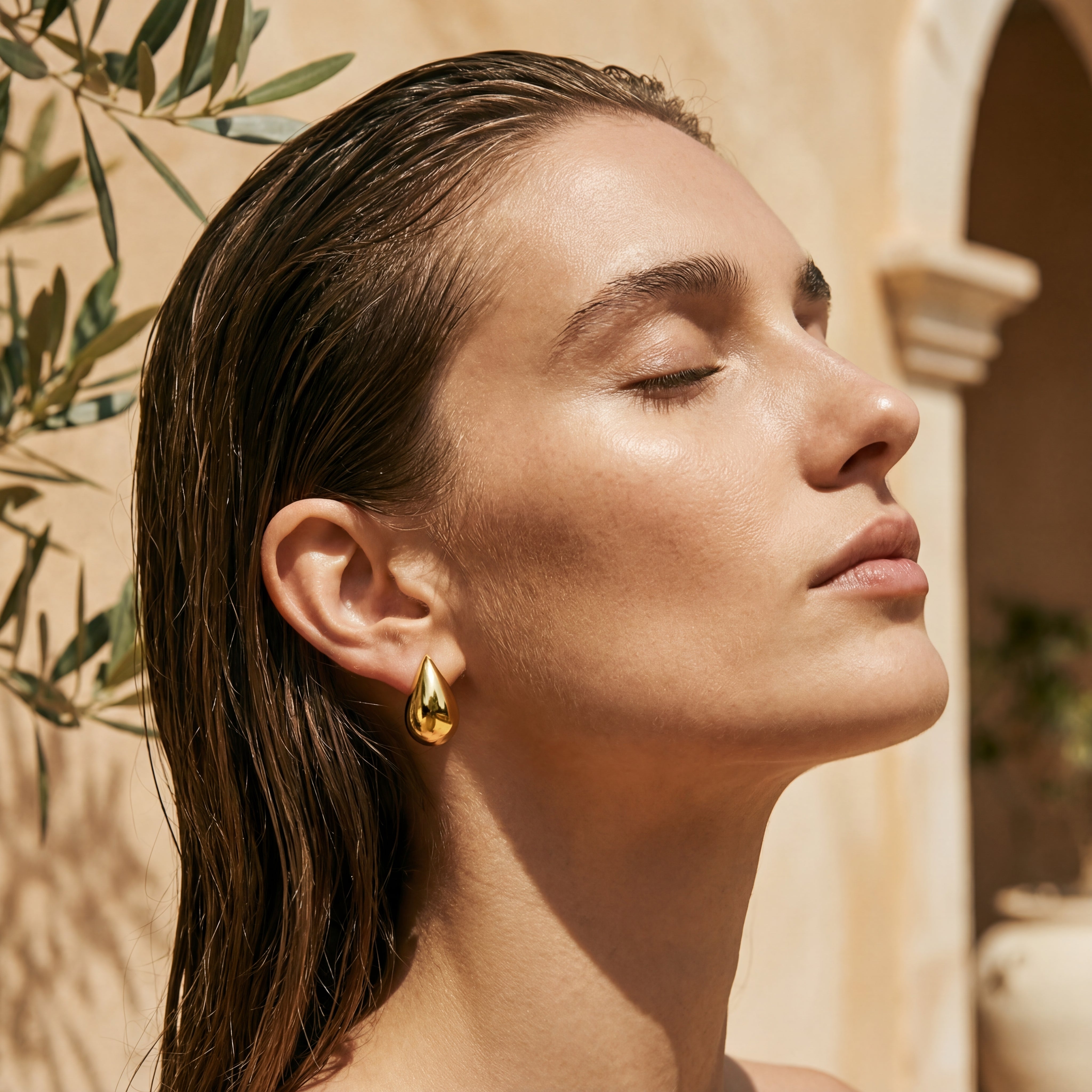 Femme portant les boucles d’oreilles Éclat dorées en acier inoxydable 316L – forme goutte bombée, bijou sculpté et lumineux, waterproof et hypoallergénique