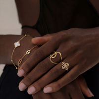 Bijoux Soreli portés sur main féminine : Bague Volute dorée en acier inoxydable avec bague trèfle pavée et bracelet raffiné, waterproof, hypoallergénique, ne ternissent pas.