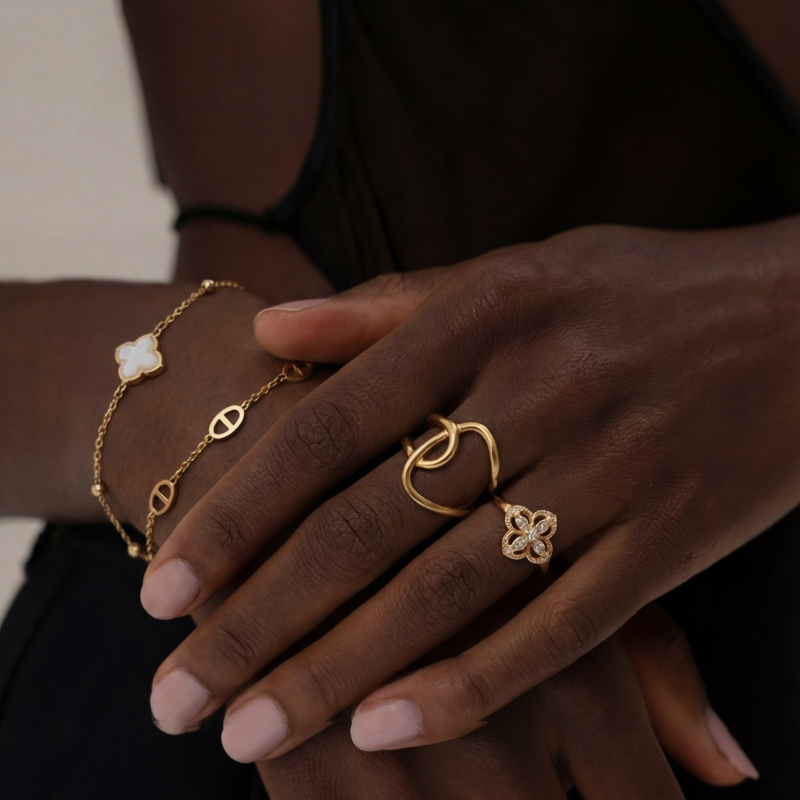 Bijoux Soreli portés sur main féminine : Bague Volute dorée en acier inoxydable avec bague trèfle pavée et bracelet raffiné, waterproof, hypoallergénique, ne ternissent pas.