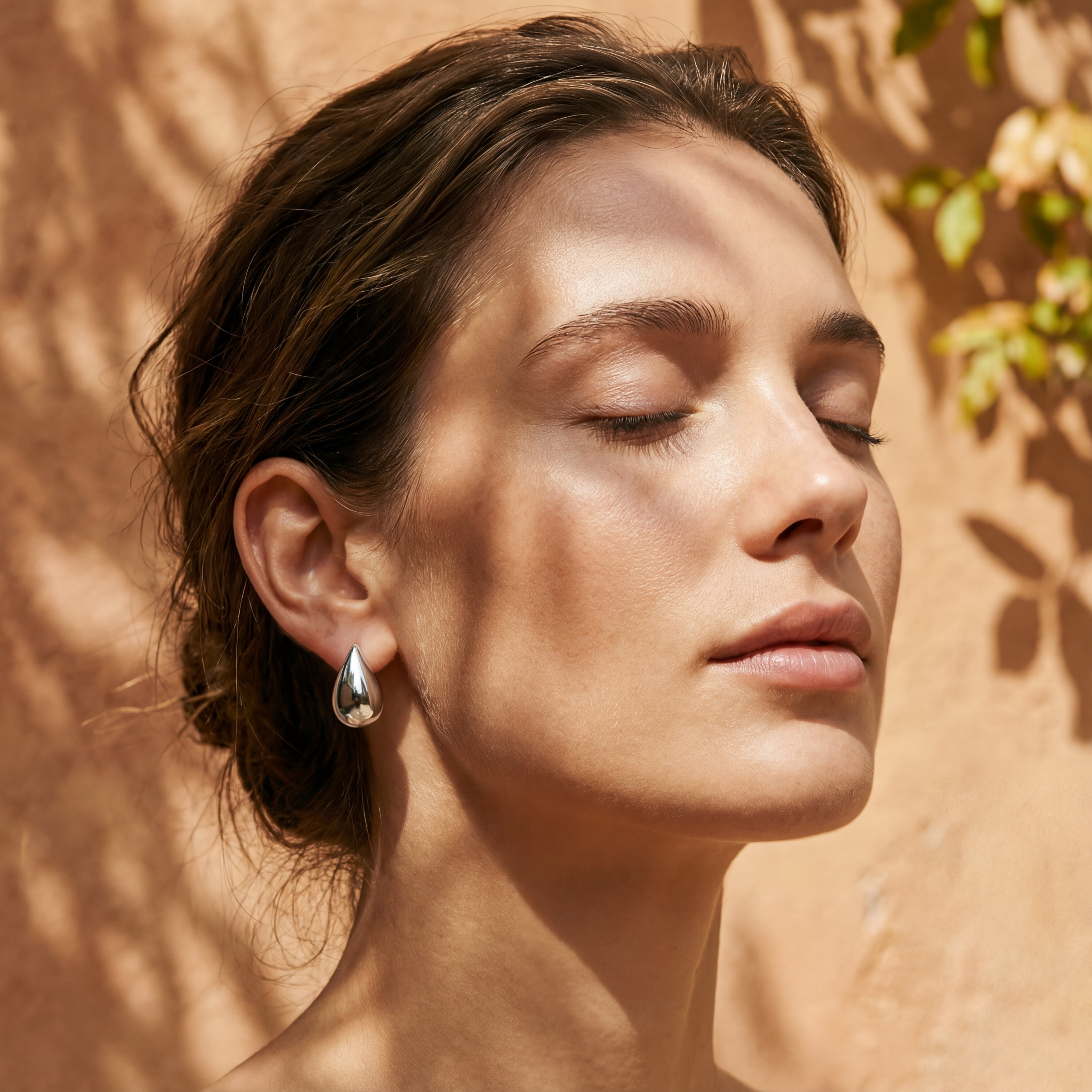 Femme portant les boucles d’oreilles Éclat argentées de Soreli Paris, prises en lumière naturelle, mettant en valeur leur finition en acier inoxydable brillant.